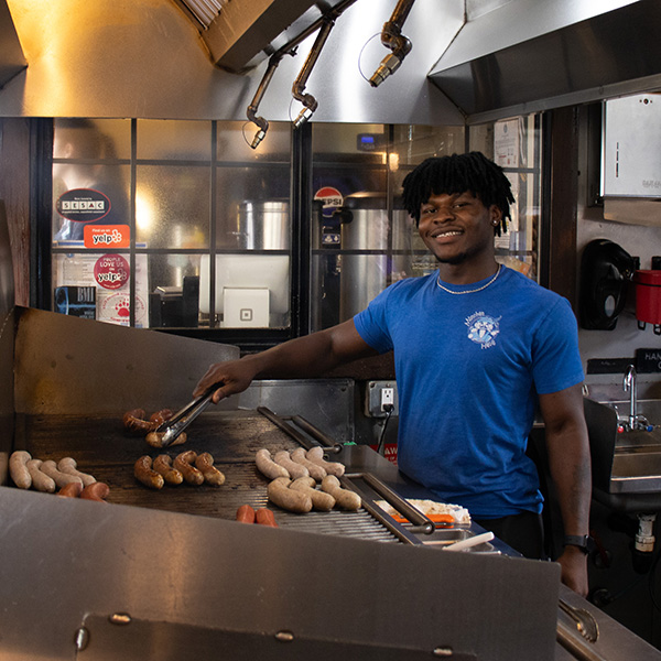München Haus employee standing at the grill cooking german sausages.